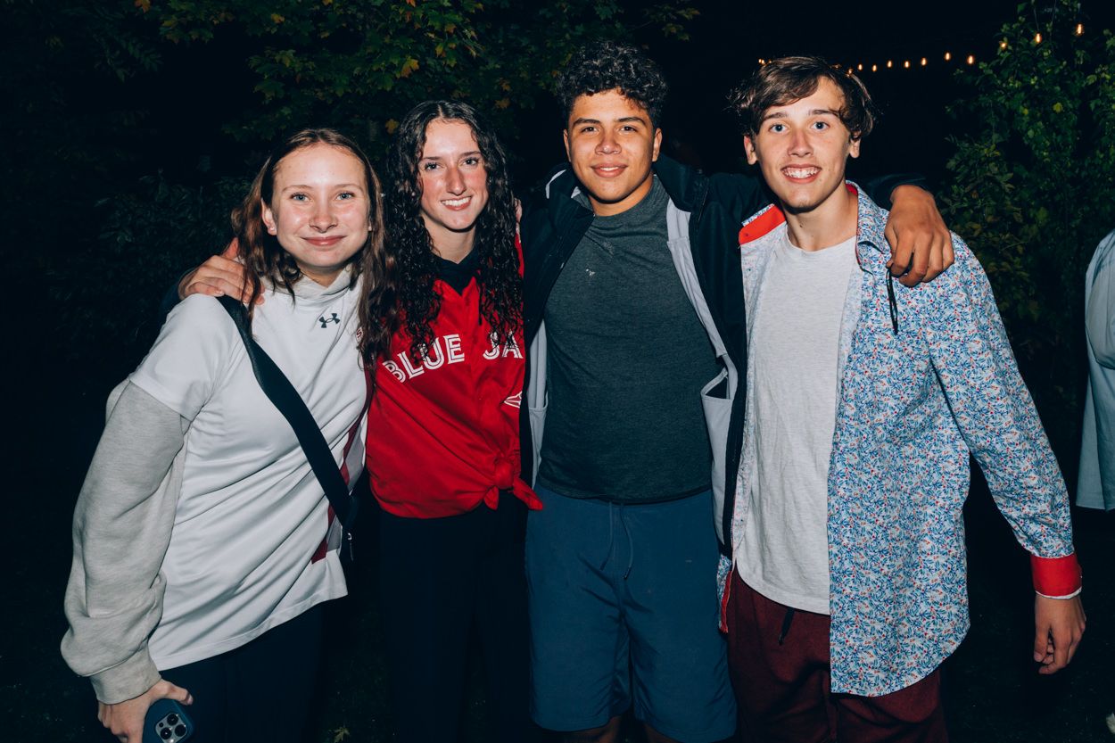 Friends posing together at a nighttime outdoor gathering with string lights visible in the background.