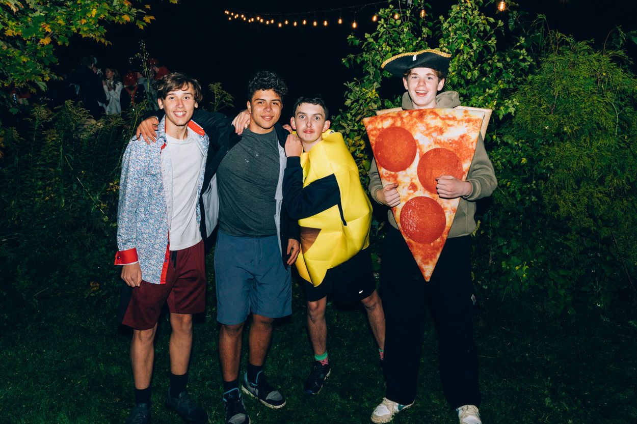 Friends pose outdoors with one wearing a pizza slice costume and another in a banana costume.