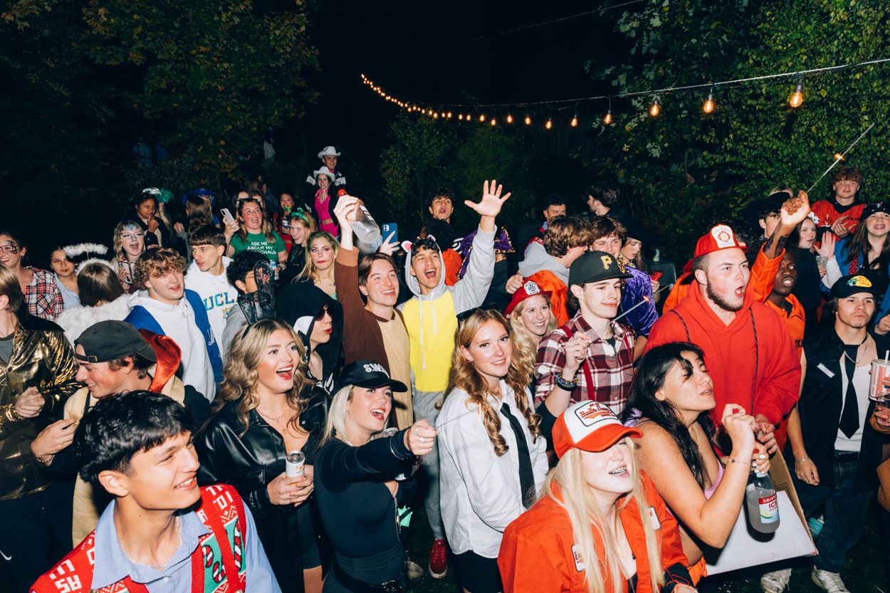 A lively outdoor party crowd celebrates under string lights at night.