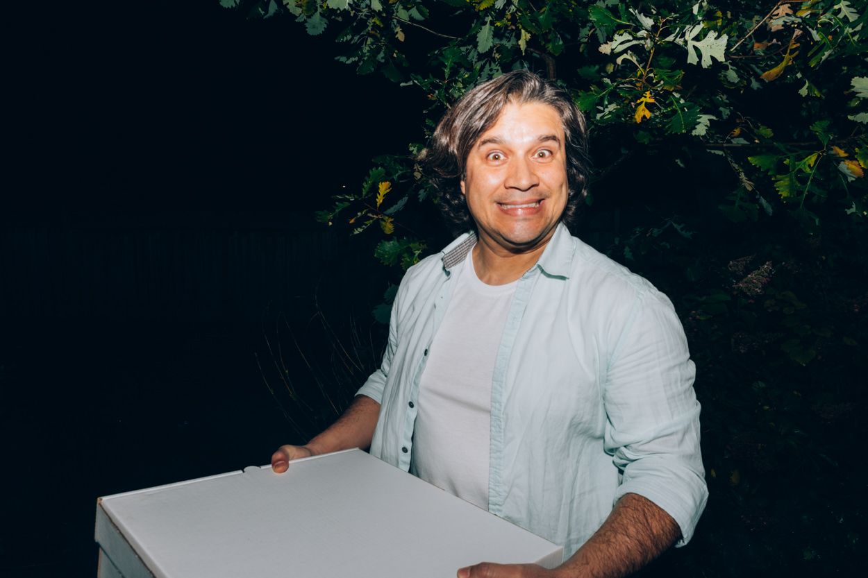 Person in light colored shirt smiling while holding a white box at night.