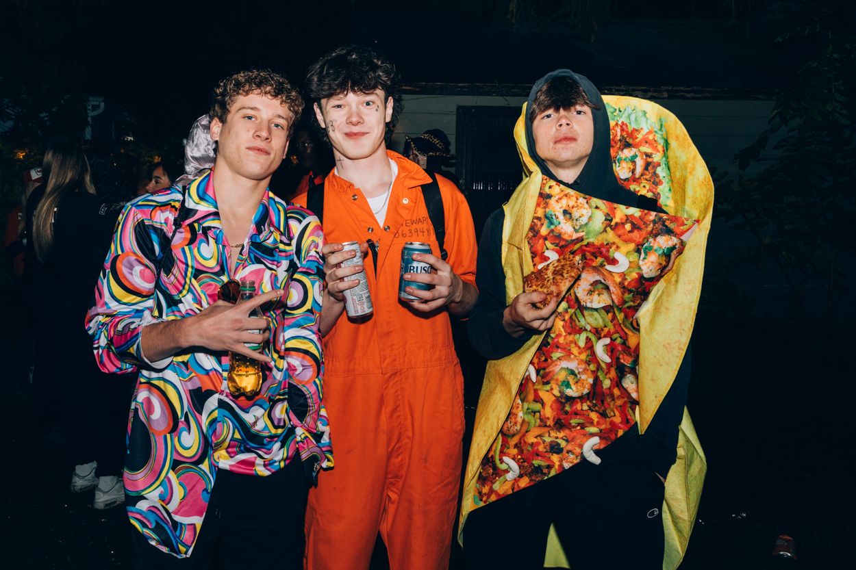 Three people in vibrant costumes including an orange jumpsuit and a taco costume at a party.