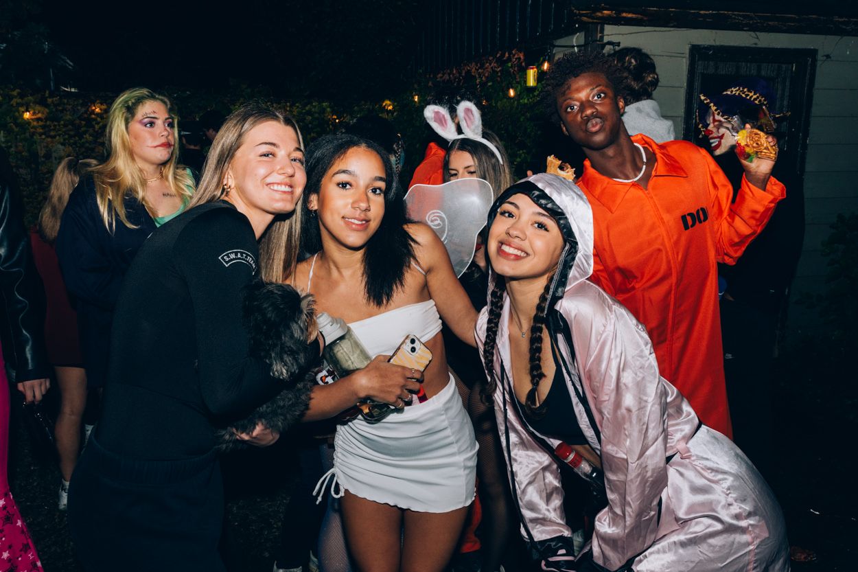 Group of friends in costumes including bunny ears pose together at a nighttime party.