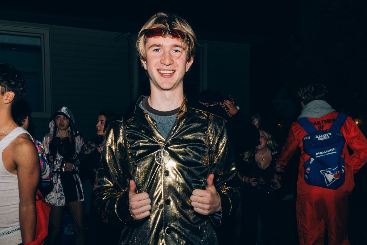Person wearing a shiny gold metallic costume gives thumbs up at a party.