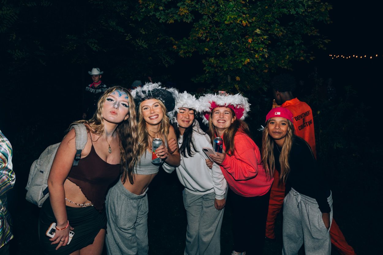 Group wearing matching white fuzzy hats posing together at a nighttime outdoor party.