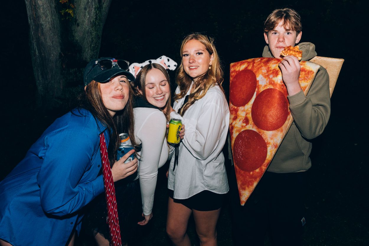 A group of friends at a costume party with one person wearing a large pizza slice costume.