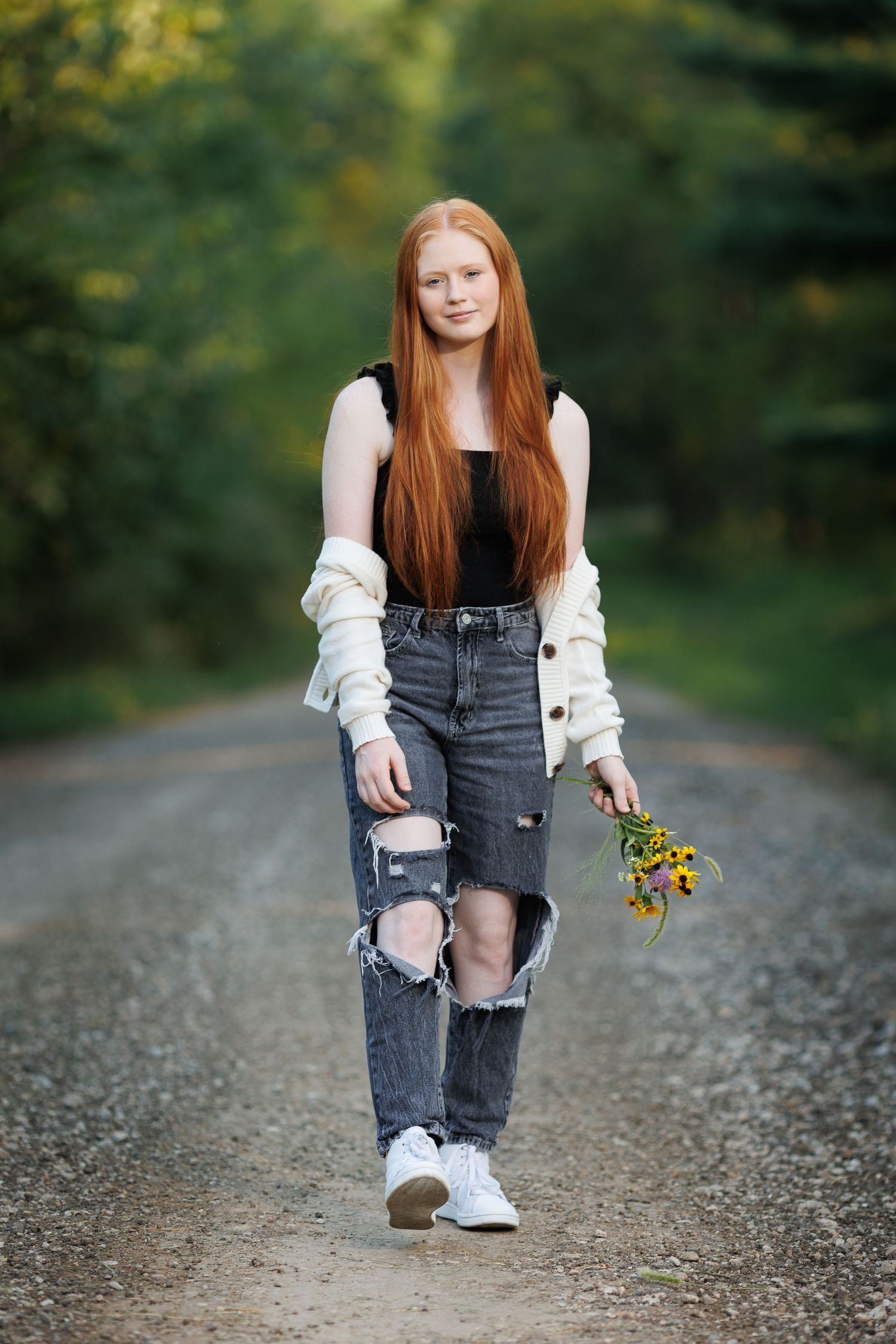 Gorgeous Illinois high school senior walking down a rock road in the woods carrying wildflowers.