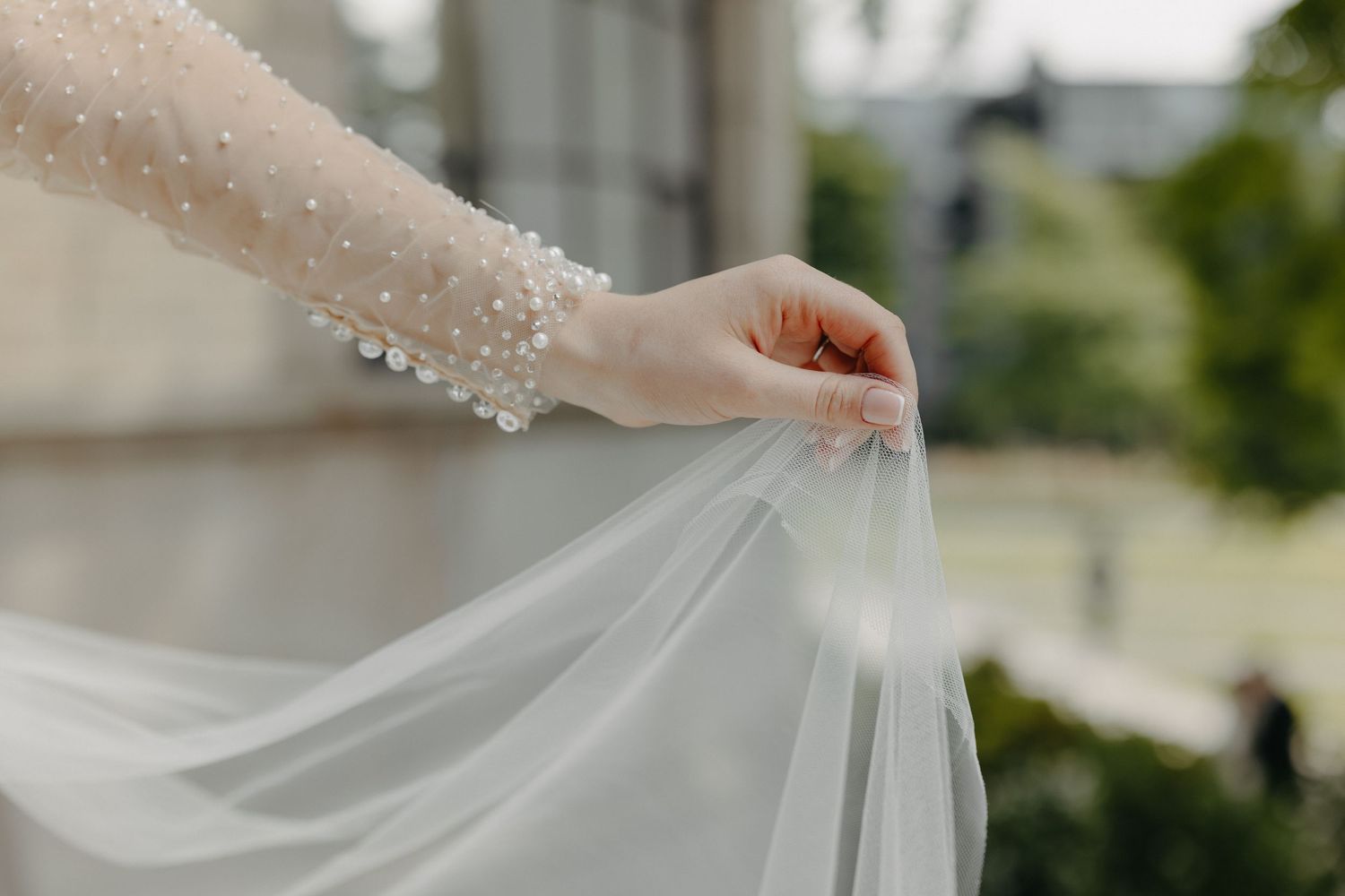 Close-up detail of delicate beaded lace sleeve and flowing white wedding veil.
