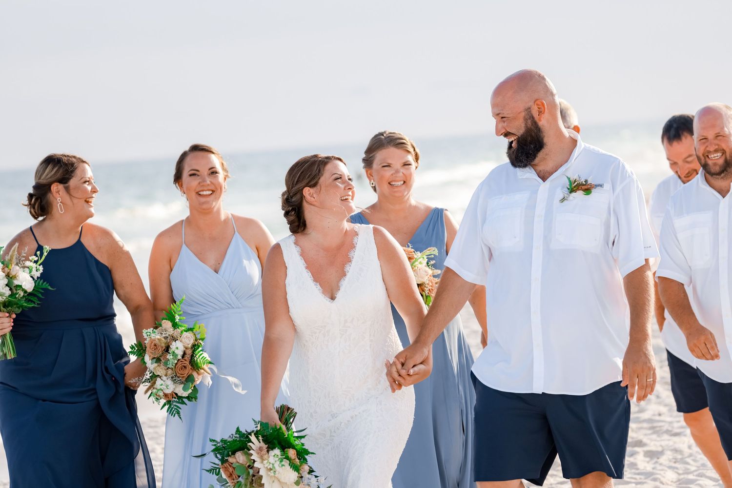 Wedding party laughing together on a sunny beach.