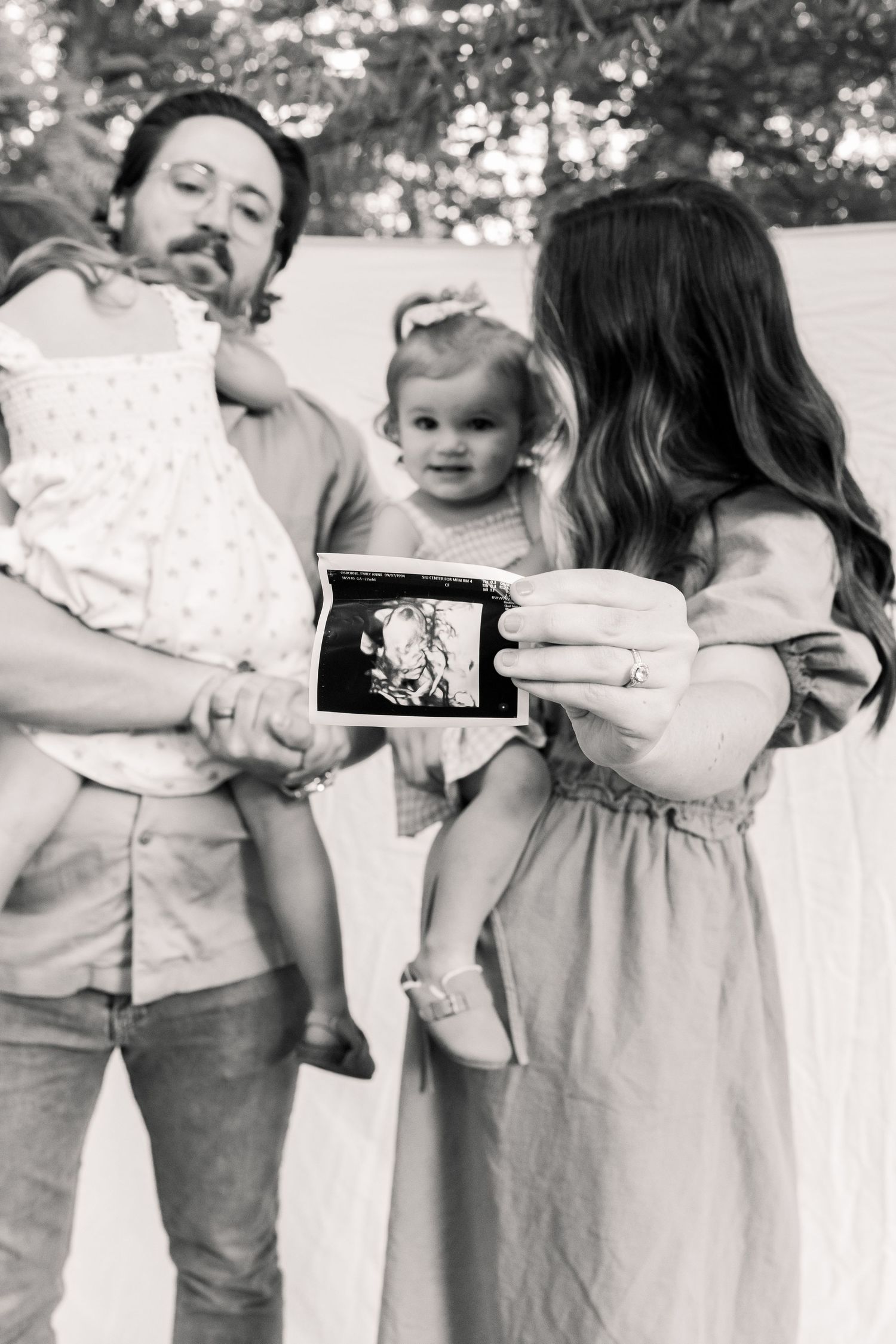 Two young children share a tender moment while looking at a phone screen together outdoors.
