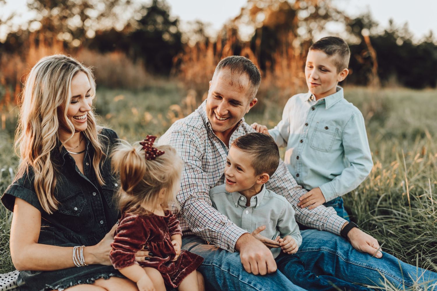 Family of five sitting together in tall grass field during golden hour.