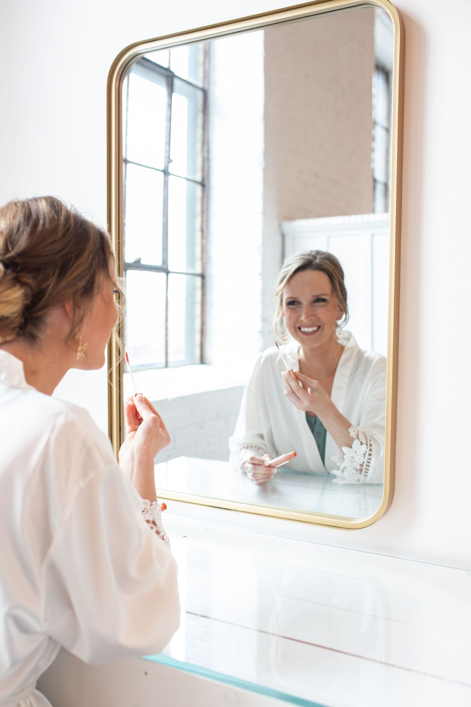 Reflection in gold-framed mirror shows preparation scene in bright white room.