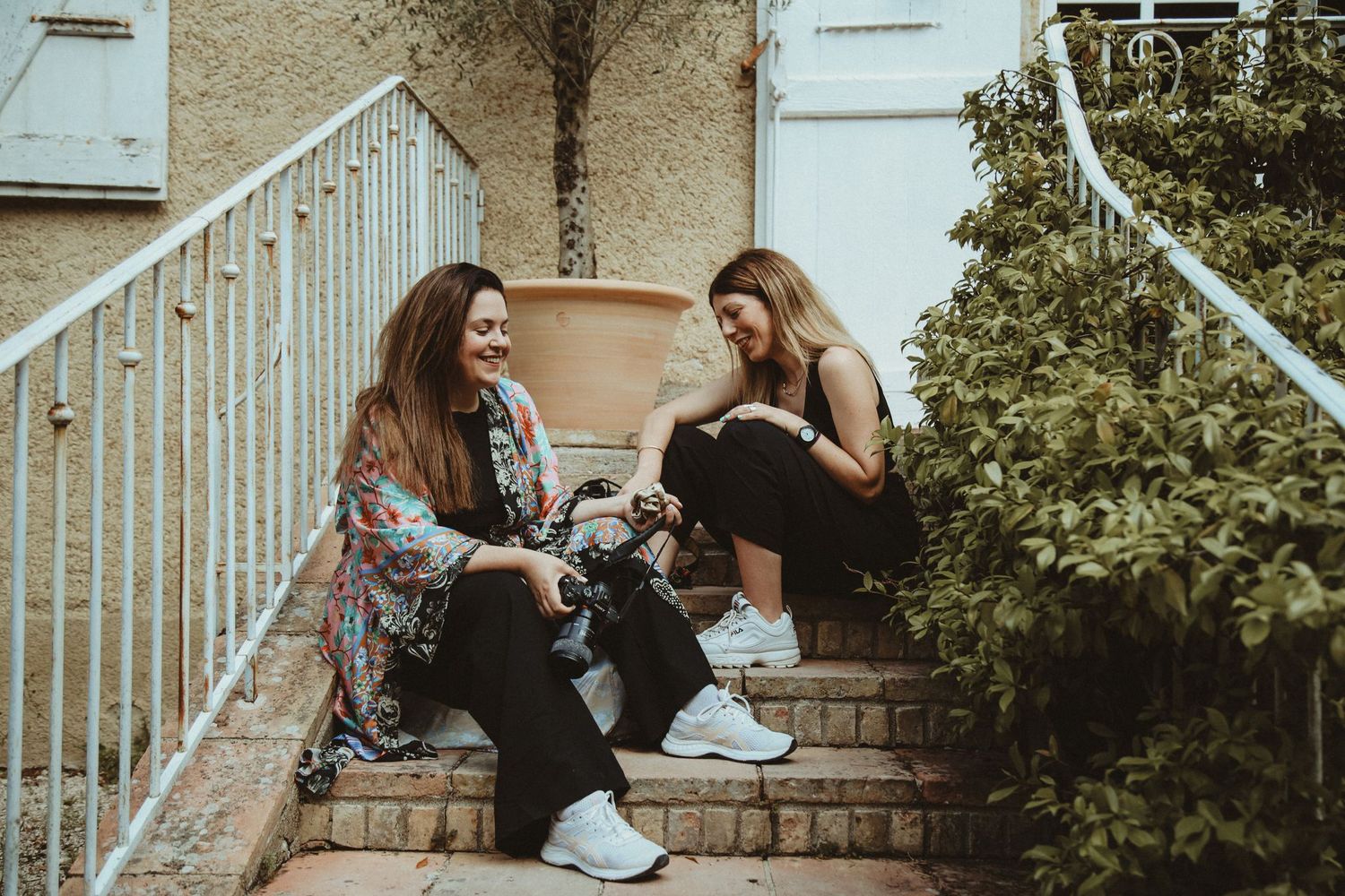 Two friends sitting on outdoor steps having a casual conversation.