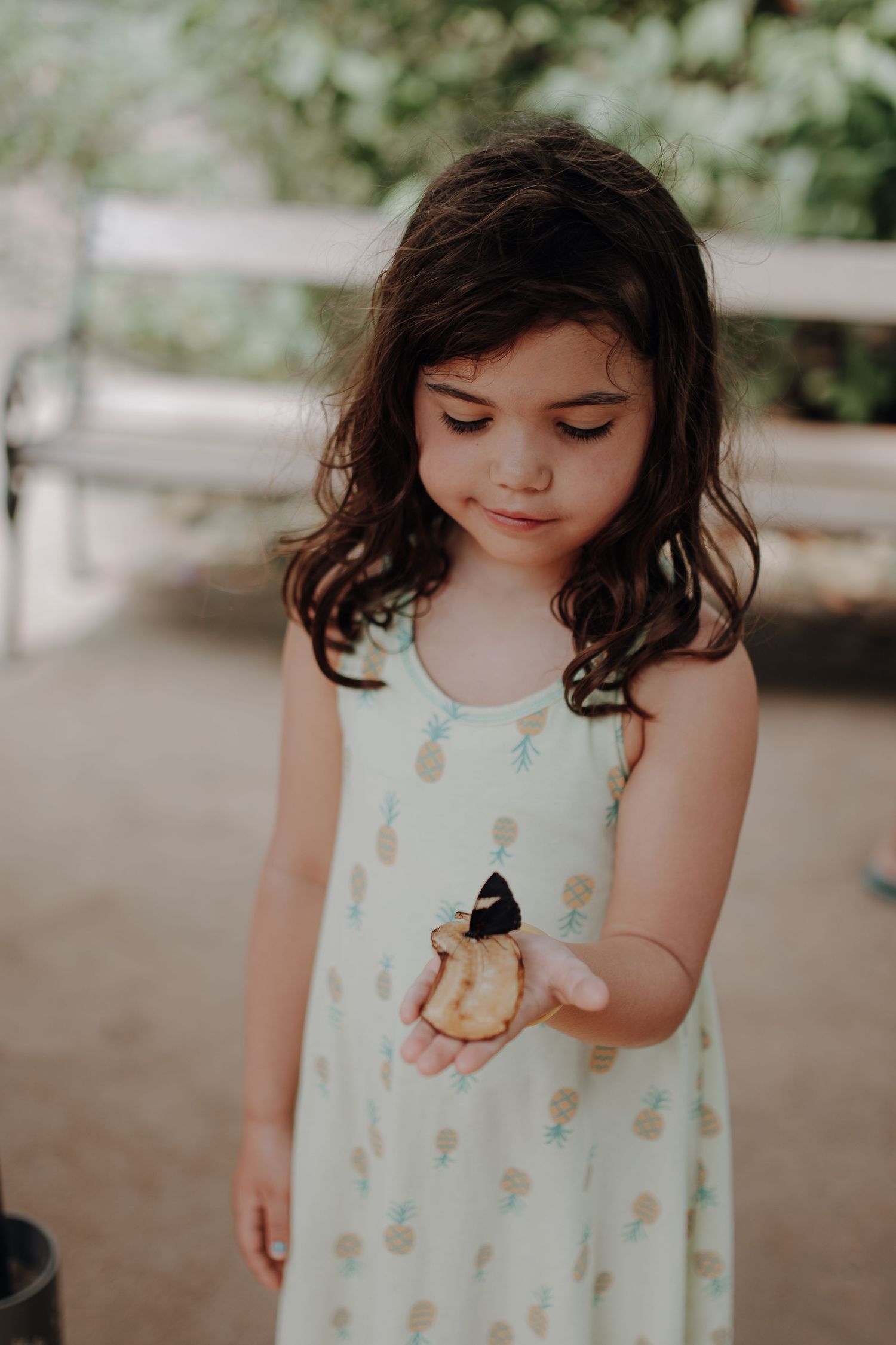 A child in a white patterned dress looks down at something small in their hand.