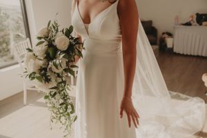 Elegant white wedding dress with cascading bouquet featuring roses and greenery.
