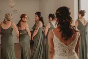 Bridesmaids in sage green dresses gather together during wedding preparations.