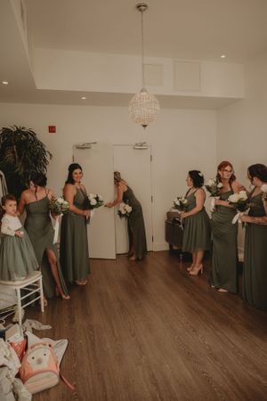 Bridal party in sage green dresses gathered in a room with crystal chandelier.
