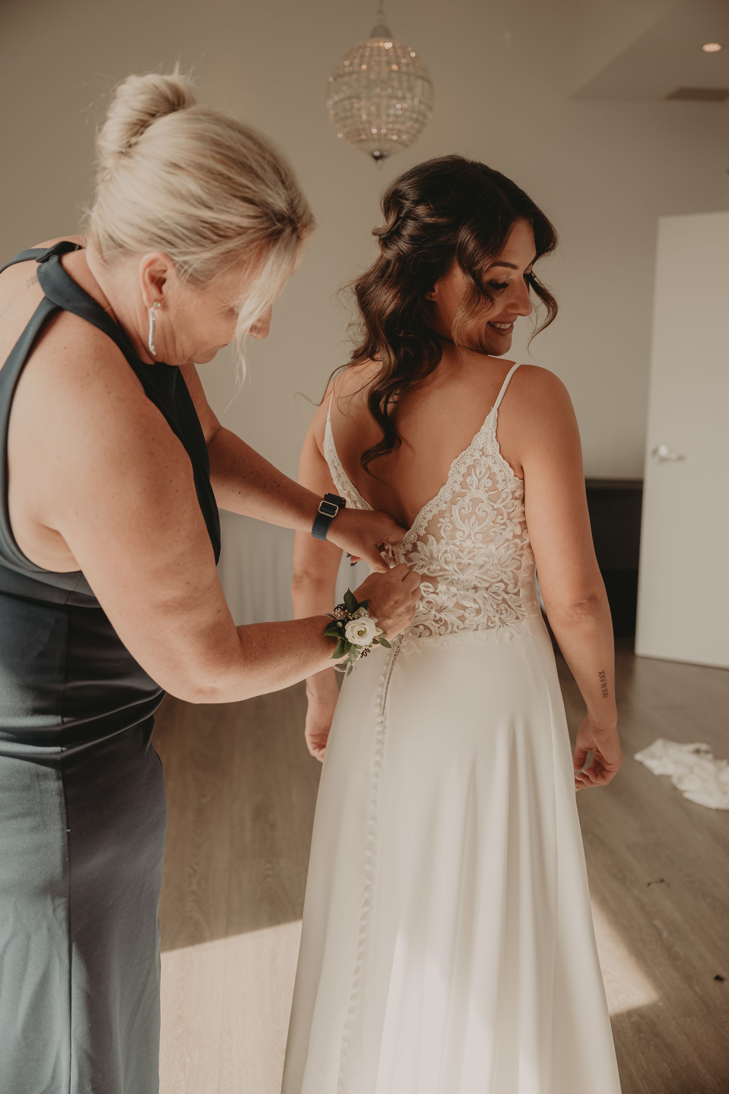A wedding dress being buttoned up in a room with a crystal chandelier.
