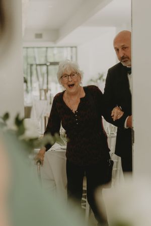 Two wedding guests in black attire sharing a joyful moment at an indoor reception.