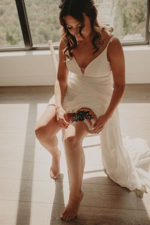 Wedding dress detail shot showing the application of a garter in warm natural lighting.