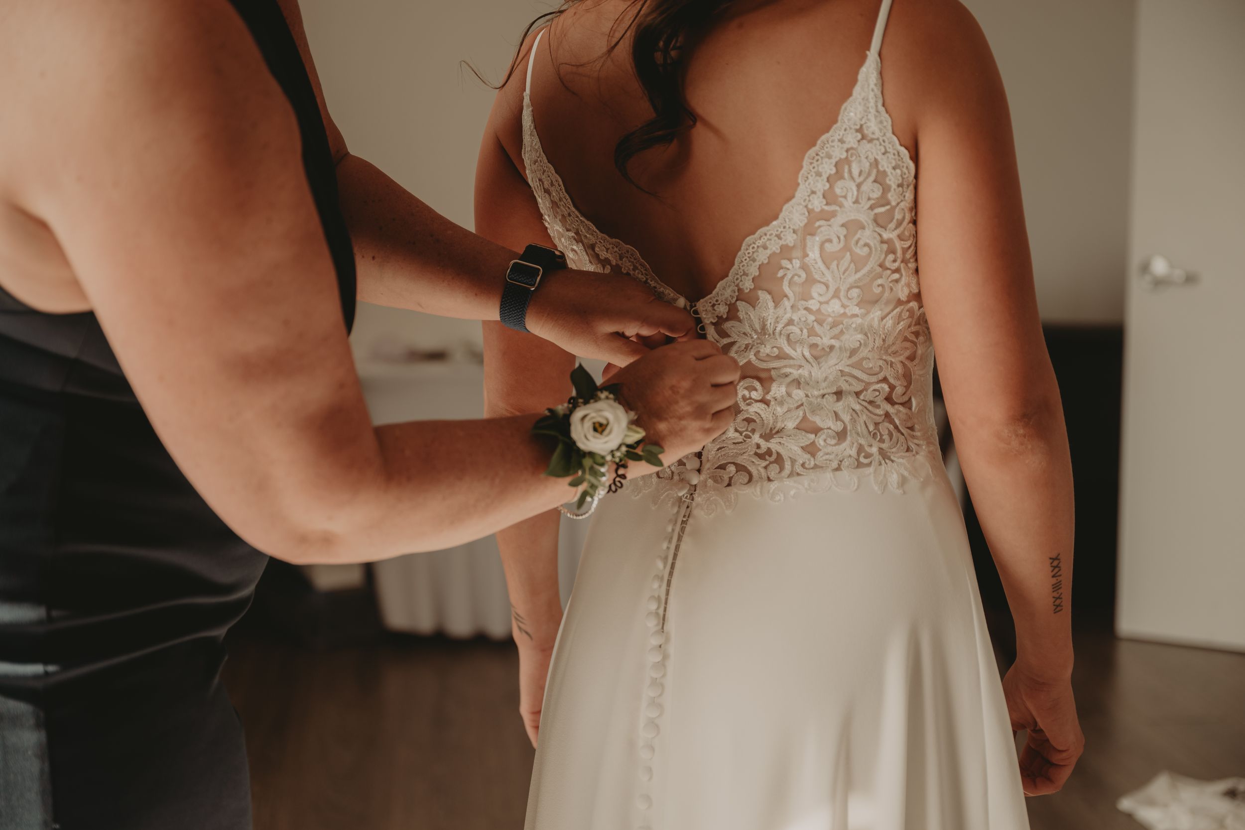 Close-up of intricate buttons being fastened on the back of a white wedding dress.