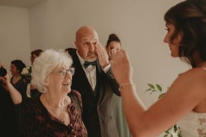 Warm candid moment during wedding ceremony with guests in background.