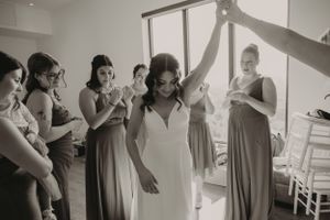 Emotional wedding preparation scene with bridesmaids in sage dresses celebrating a special moment together.