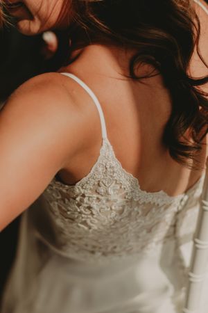 Close-up of delicate lace detailing on a white wedding dress strap against a warm-toned background.