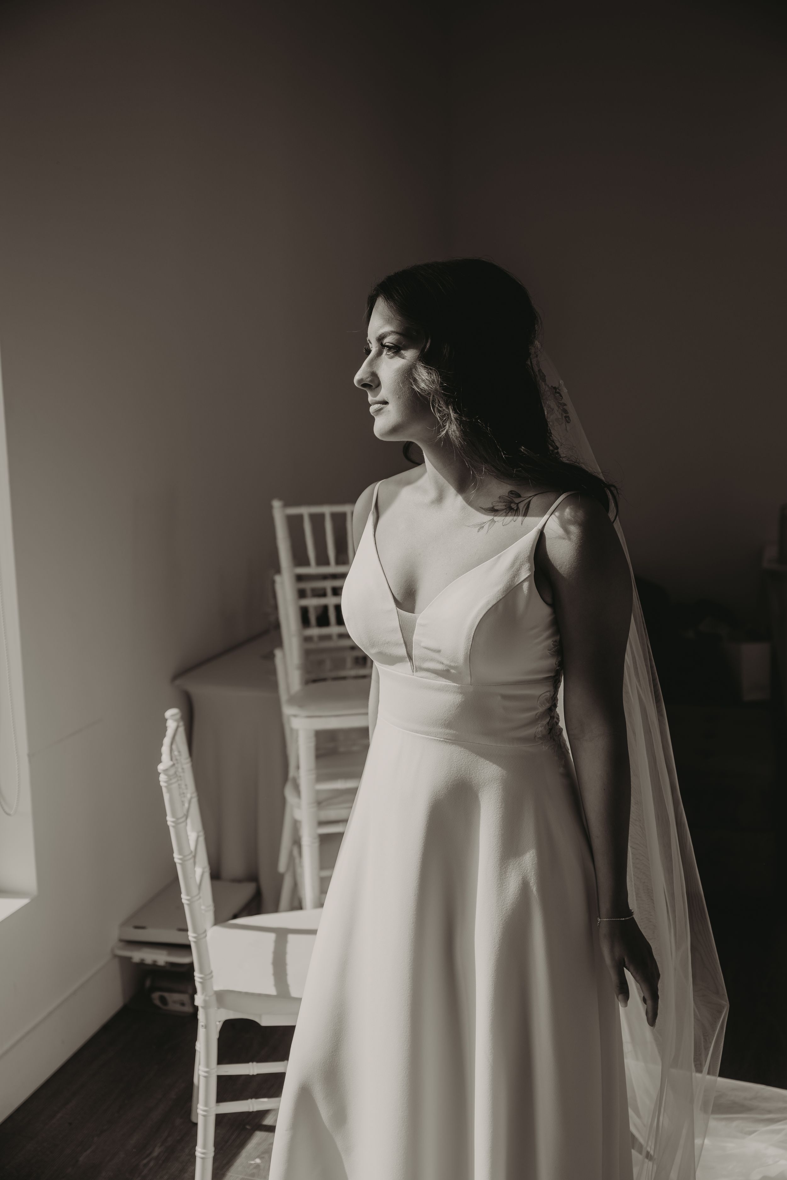 Dramatic portrait of bride in flowing white gown with veil against dark background.