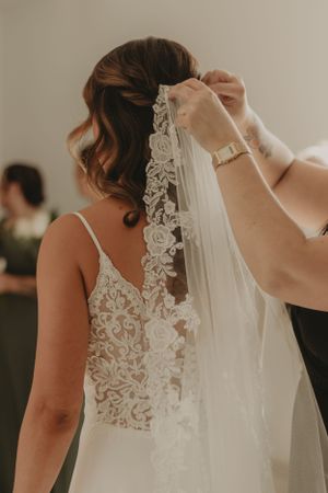 Wedding dress preparation showing intricate lace detail and veil being attached.