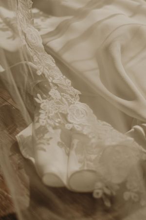 Detailed shot of white lace wedding shoes with floral embellishments and veil.