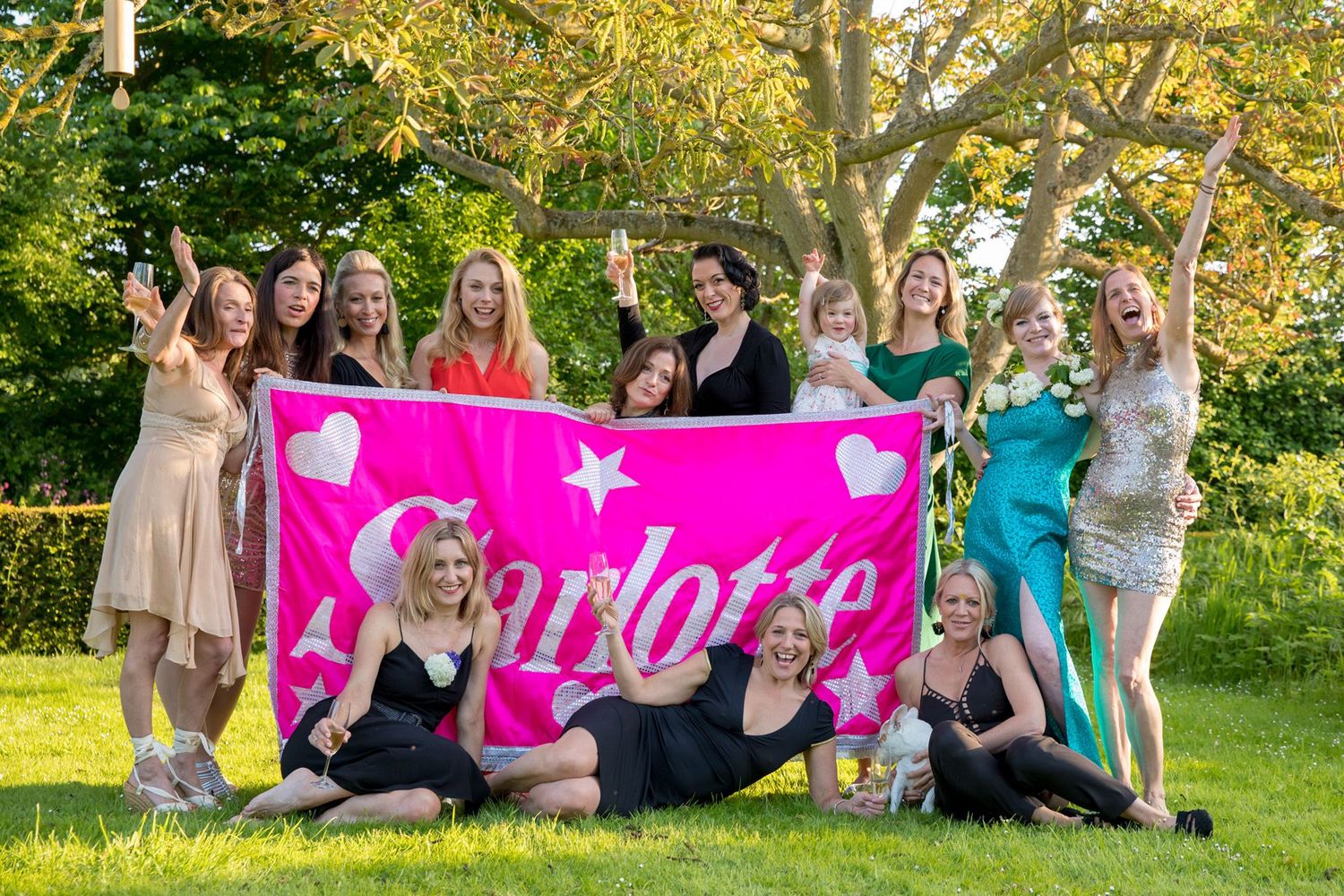 A group of friends pose with a pink banner during an outdoor celebration.