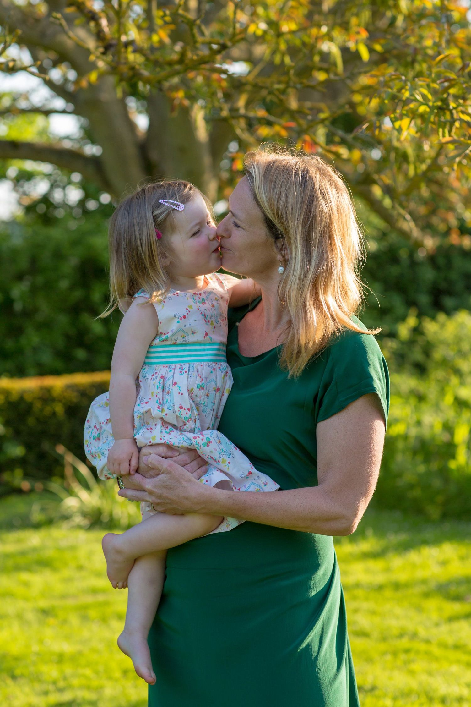 A tender moment captured outdoors with golden sunlight filtering through trees.