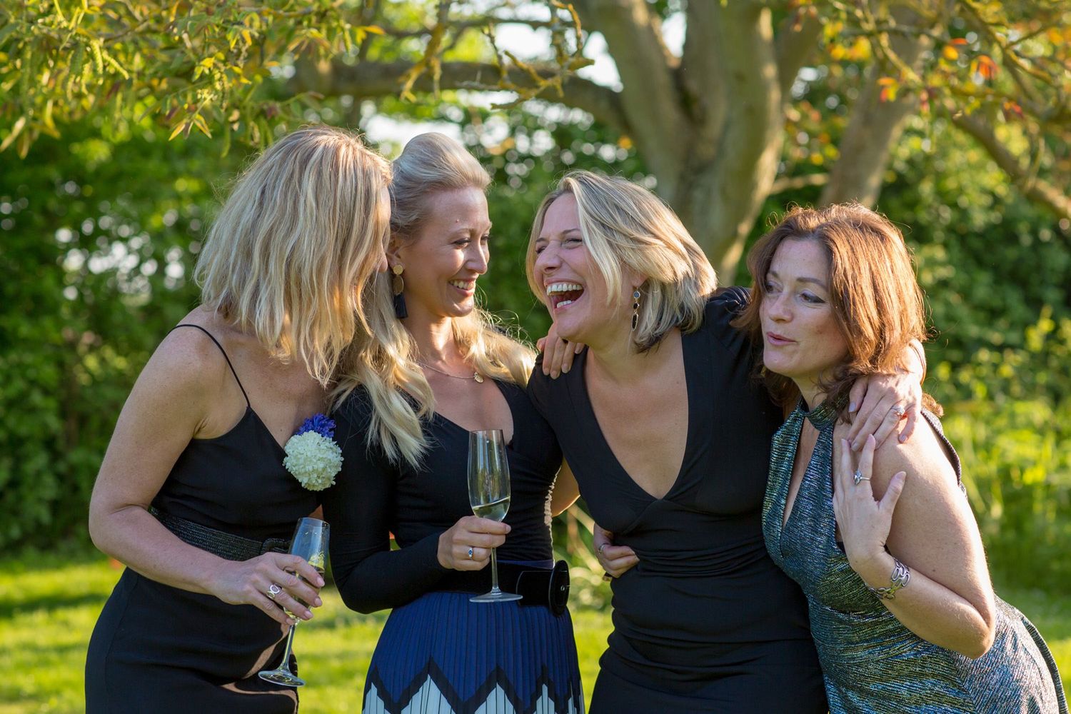 Friends sharing laughter during an outdoor celebration in black dresses.