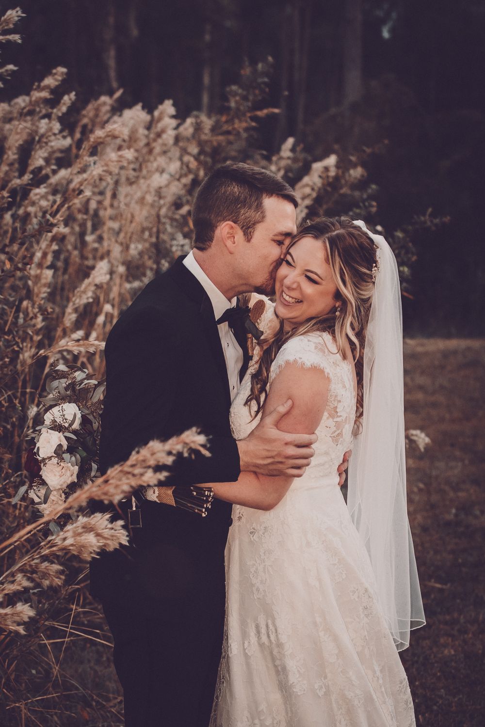 A romantic wedding portrait of newlyweds embracing among tall grass at sunset.