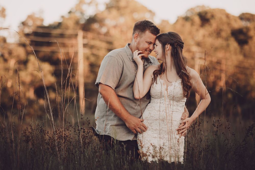 Romantic golden hour photo of a couple embracing in a field wearing white lace dress and casual attire.