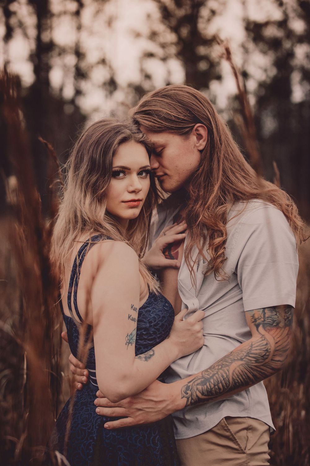 Romantic portrait of a couple in navy and white clothing embracing in a field at sunset.