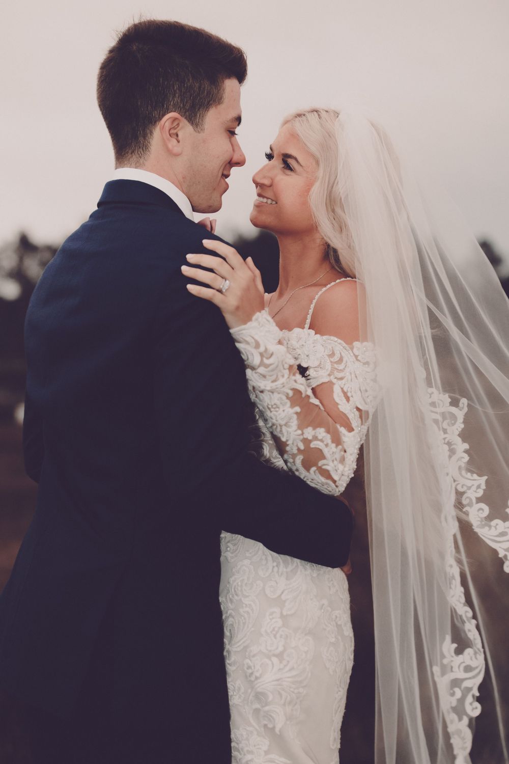 A romantic wedding portrait of newlyweds embracing outdoors at dusk.