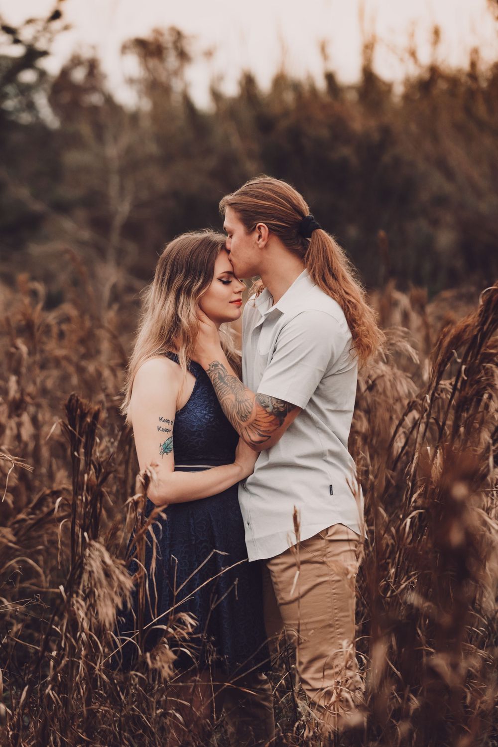 Intimate portrait of a couple in navy and white attire standing close in tall grass during sunset.