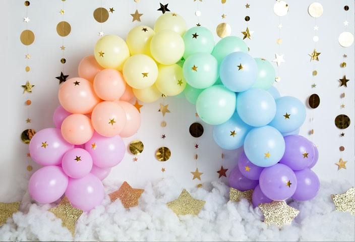 Pastel rainbow balloon arch with gold stars and cotton cloud base against white background.