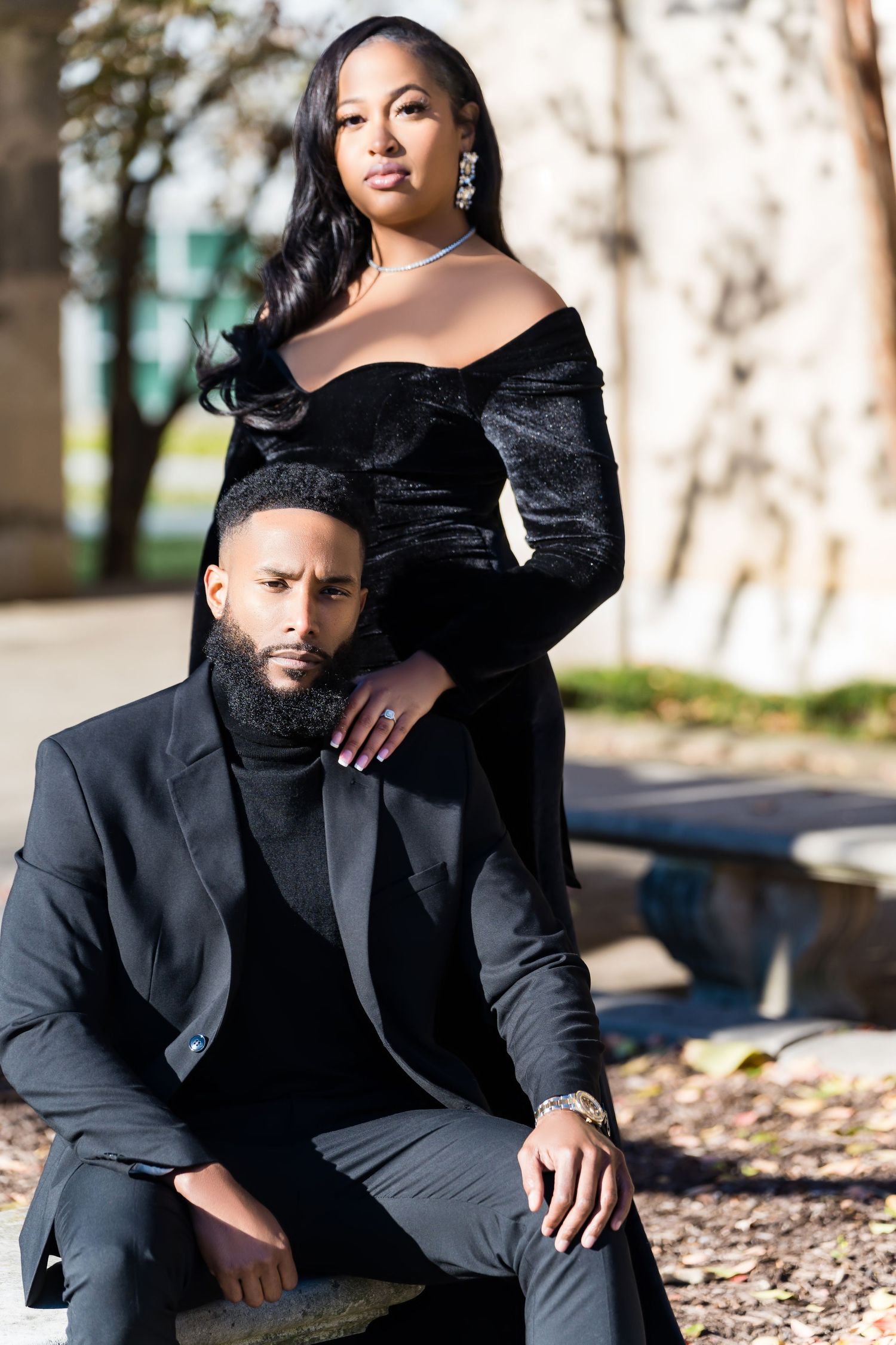 A stylish couple in black formal wear poses for an artistic outdoor portrait.