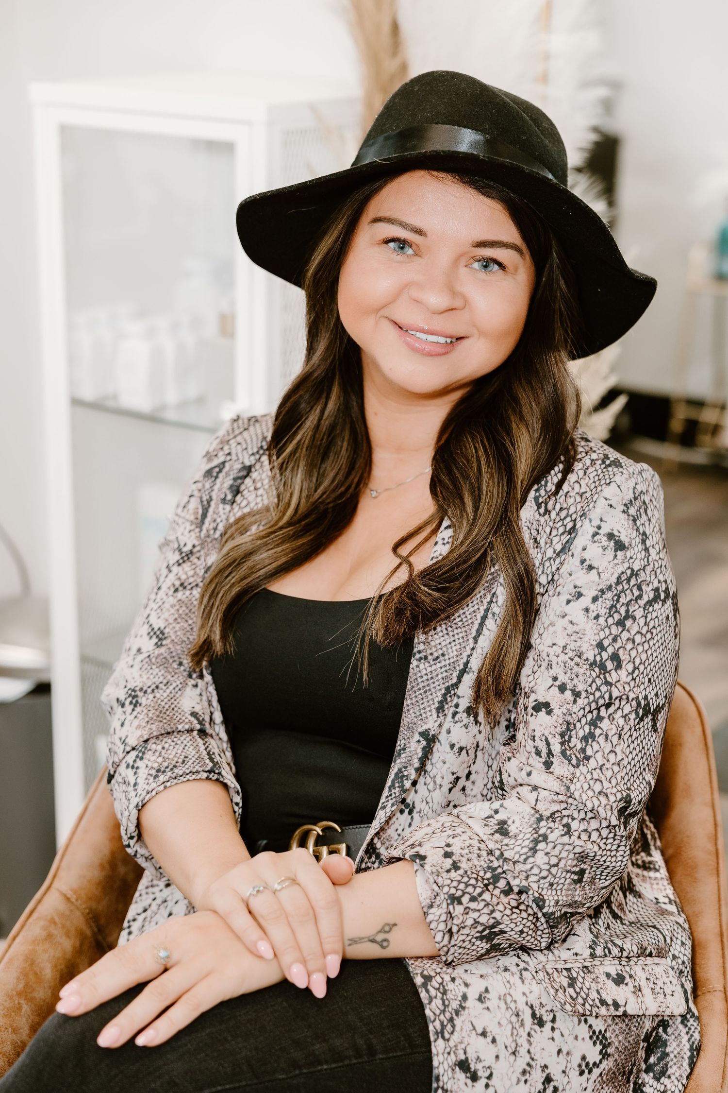 A person sitting in a salon chair wearing a snakeskin print jacket and black hat.