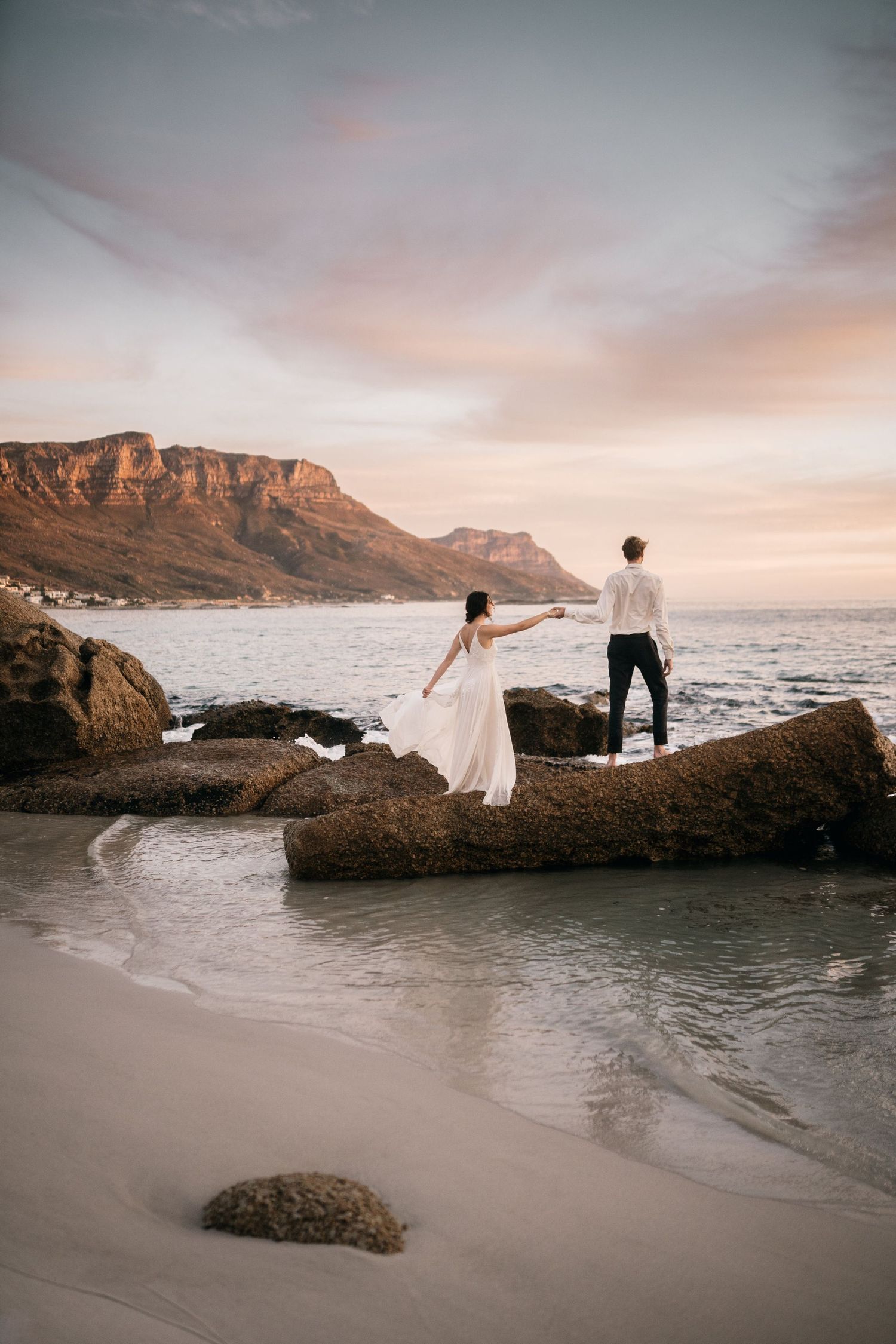 Romantic seaside photoshoot at sunset with dramatic coastal cliffs.
