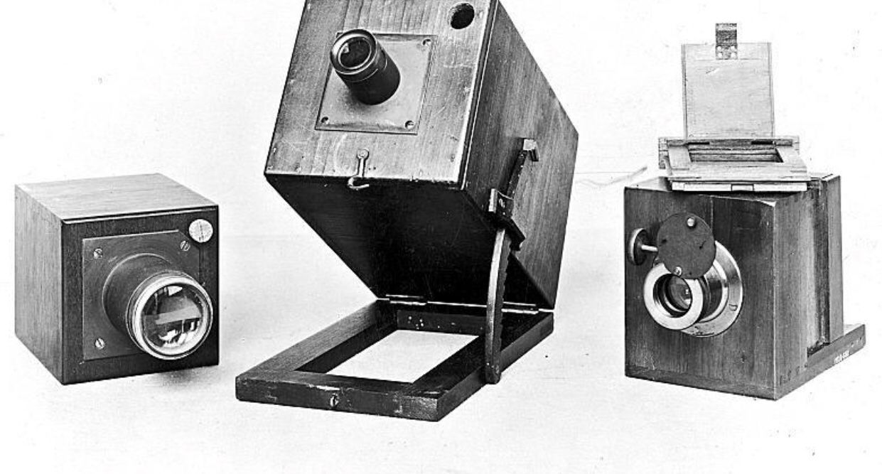 Collection of three vintage wooden box cameras from early photography history.