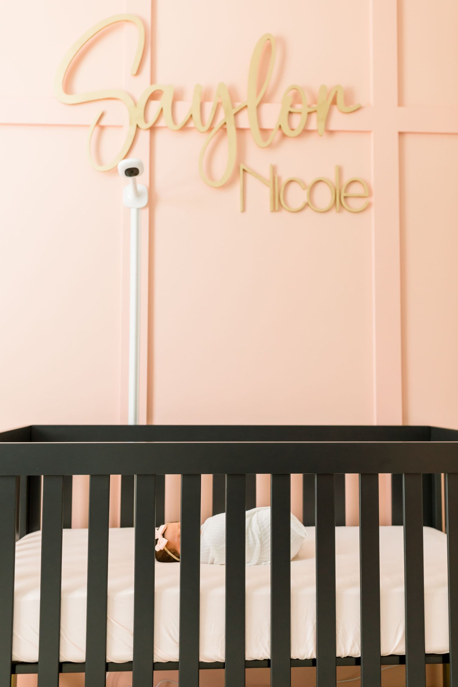 Close-up of black crib with gold cursive name sign mounted on pink wall.