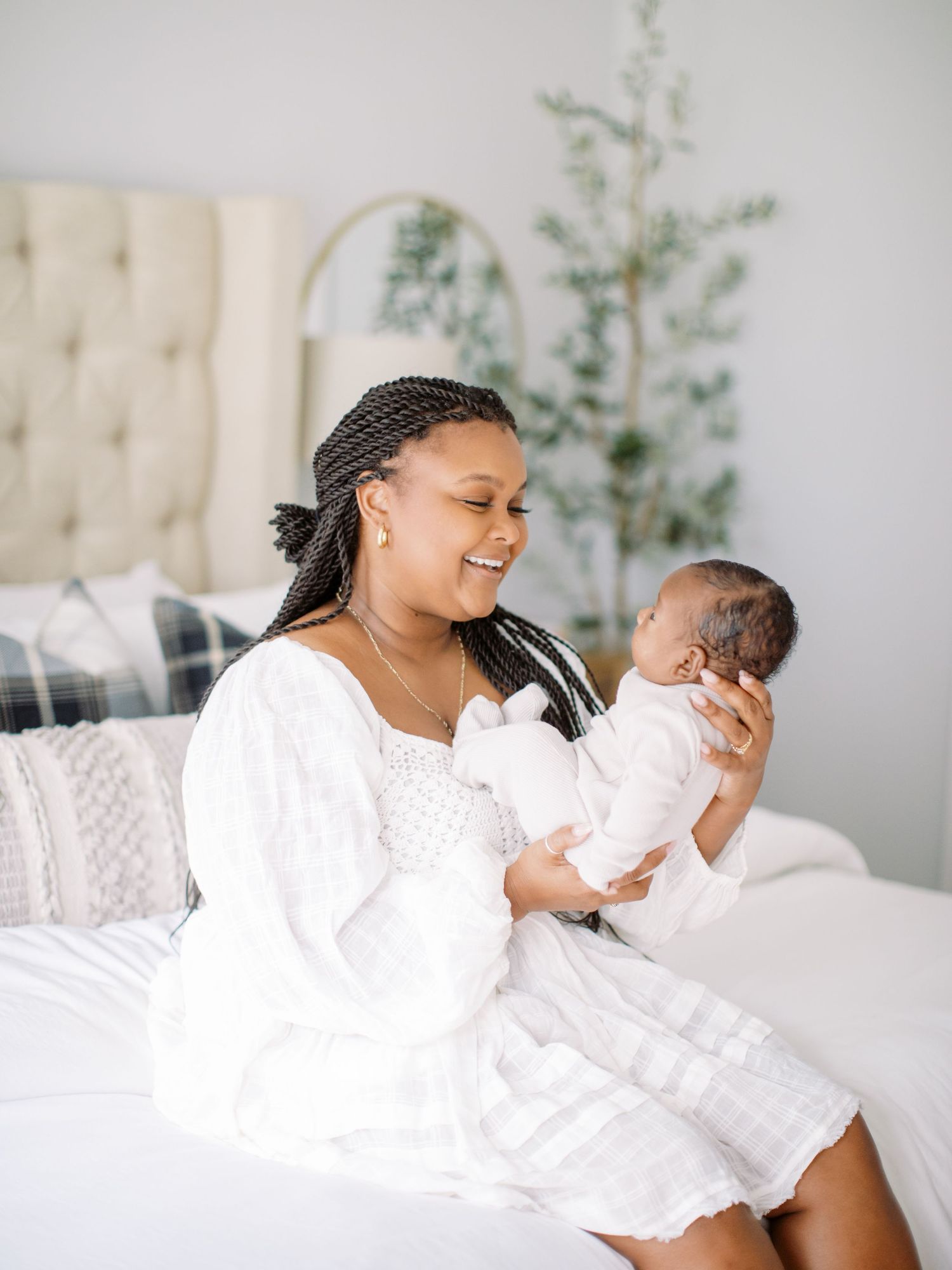 Joyful moment between parent and newborn baby, both dressed in white, on a cozy bed.