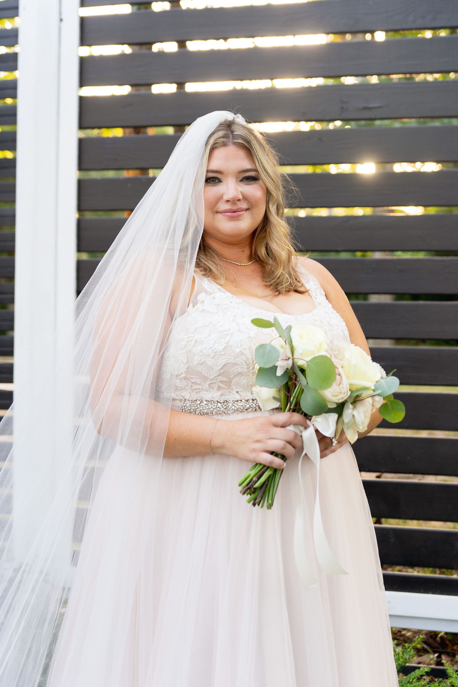 Radiant bride in white beaded gown poses with bouquet against modern black slatted wall.