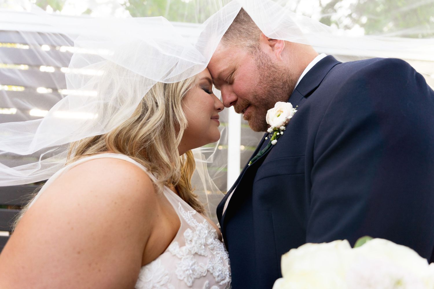 Tender moment between newlyweds as veil flows in gentle breeze.