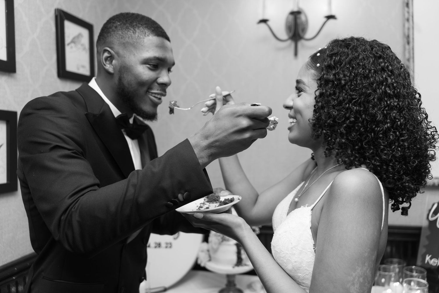Wedding couple shares playful cake-feeding moment in black and white photography.