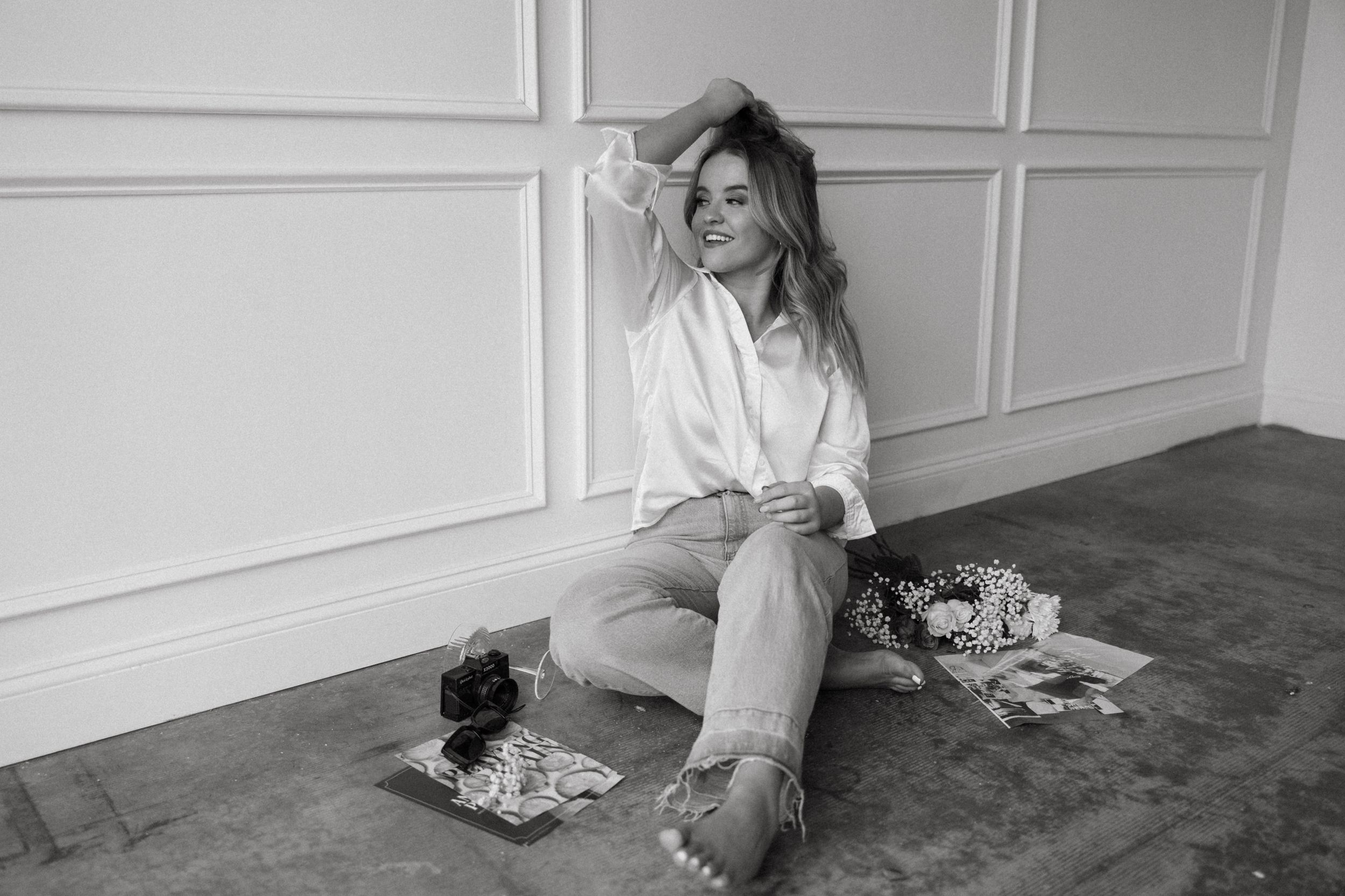 Artistic black and white photo of figure lounging on studio floor against white paneled wall.