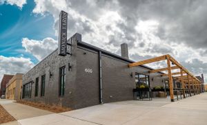 Industrial style building exterior with gray facade and wooden pergola outdoor seating area.